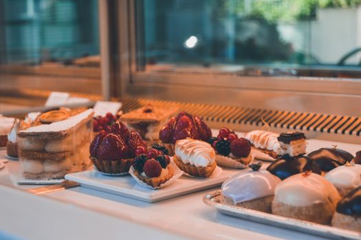 Vitrine de pâtisserie avec des desserts variés, incluant tartes aux fruits, éclairs et gâteaux élégants.