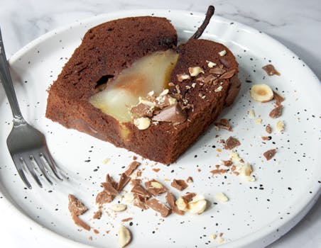 Gâteau au chocolat avec poire Belle Hélène, décoré de morceaux de chocolat et d'amandes sur une assiette blanche.